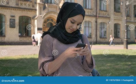 Young Sweet Muslim Girl In Hijab Is Typing Message On Smartphone And