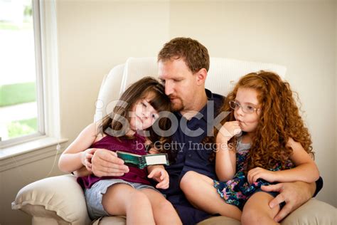 dad reading to little daughters sitting on his lap stock