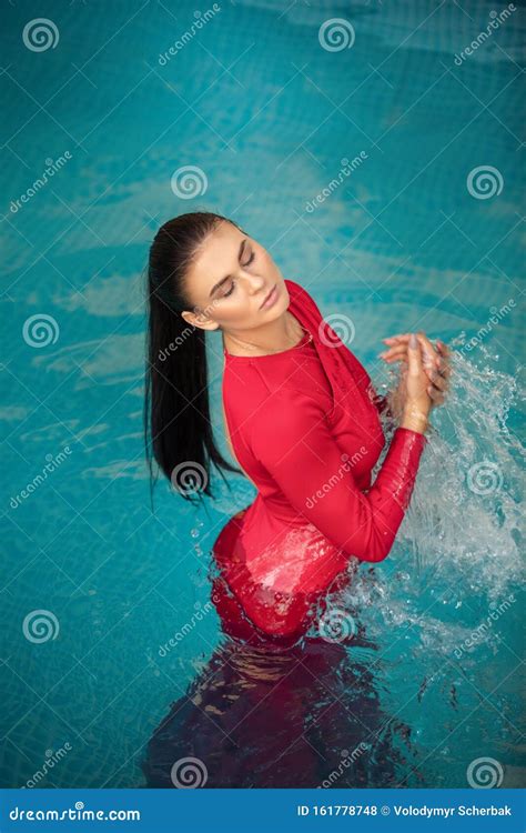 Young Woman Floating On Swimming Pool In Red Dress Beauty Shot Stock