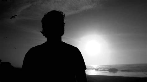 Silhouette Of Man Standing On Beach Watching Sunset Over