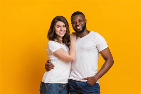 Romantic Interracial Couple Embracing And Posing Over Yellow Background