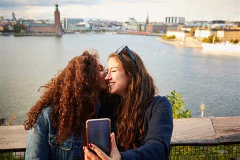 Smiling Lesbian Couple Kissing While Taking Selfie With Mobile Phone