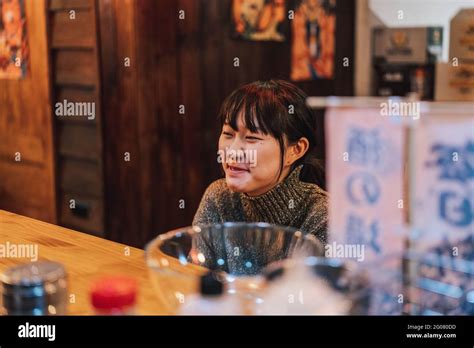 Asian Woman In Casual Wear Sitting At Wooden Counter While Waiting For