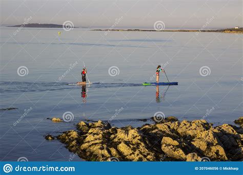 A Couple Slowly Paddle Their Surf Boards In The Calm Sea At Groomsport