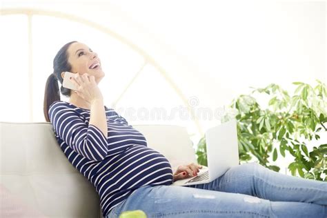 pregnant woman talking on her mobile phone and using notebook stock