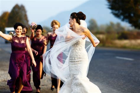 bride and funny bridesmaids run along the road in sunny evening