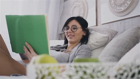 mature woman lying on couch at home reading book stock
