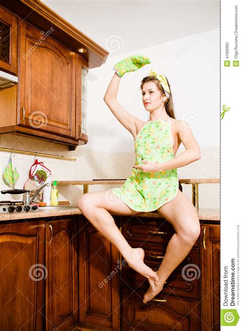dancing girl sitting on the table in the kitchen apron hand up looking at copy space on white