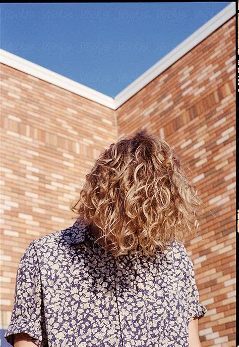 man with curly blonde hair covering his face in the sun by stocksy