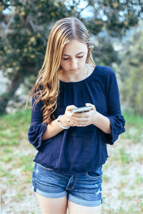 teenage girl in shorts texting on her phone by carolyn lagattuta stocksy united