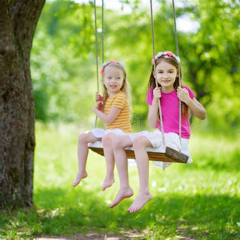 Two Cute Little Sisters Having Fun On A Swing Together In Beautiful