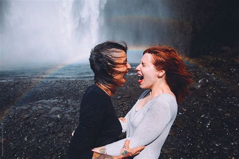couple of woman kissing in front of a waterfall by stocksy