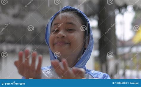 Adorable Young Asian Girl In Blue Raincoat Enjoy To Play With The Rain