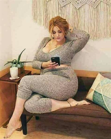 A Pregnant Woman Sitting On A Couch Looking At Her Cell Phone While