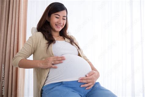 Happy Pregnant Asian Woman Touching Her Big Belly While Sitting Stock