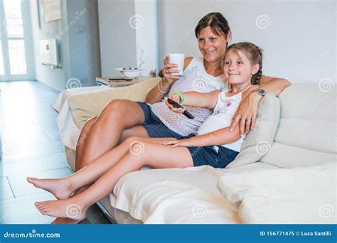 Mother And Her Daughter Are Watching Tv While Sitting On A Couch At