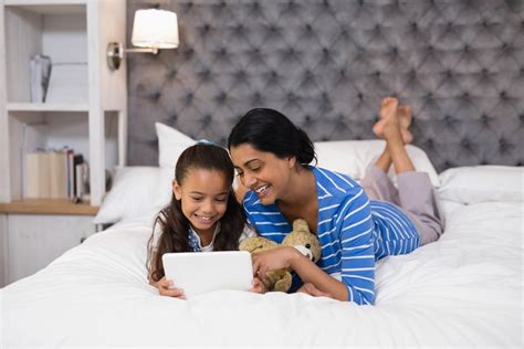 Mother And Daughter Using Digital Tablet While Lying On Bed At Home