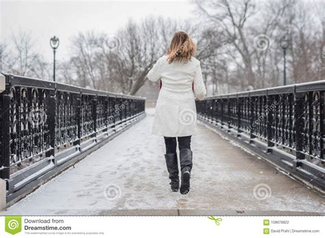 woman walking across ornate iron bridge in city park in winter w stock