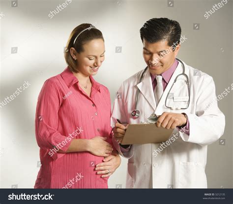 Asian American Male Doctor Consulting With Pregnant Caucasian Woman
