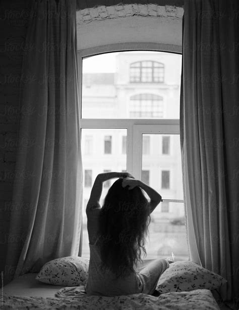Back View Of A Woman Sitting On Bed Against Window By Stocksy