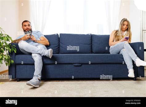 scolded couple sitting on opposite sides of the couch using their
