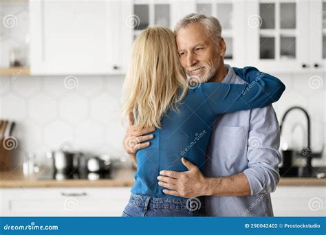 Portrait Of Romantic Elderly Couple Hugging In Kitchen Interior Stock