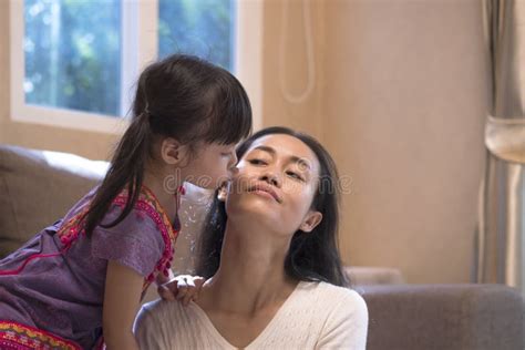 little asian girl kissing her mother`s cheek in living room at home