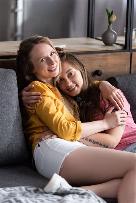 two pretty lesbians embracing while sitting on sofa in living room