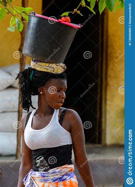 unidentified local woman carries a bucket on her head in a vill