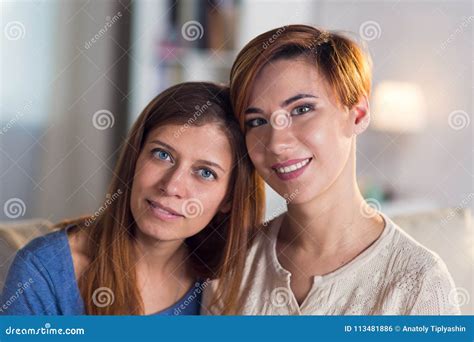 Homosexual Couple Of Lesbian Women At Home On The Couch Hugging Stock