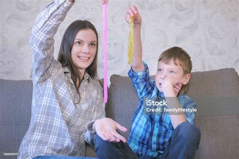 Happy Mom And Son Are Playing With Slime Sitting On The Sofa Stretching