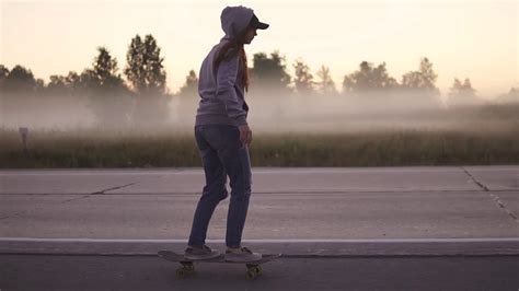 Girl Skates On A Skateboard On A Deserted Highway Against A Background