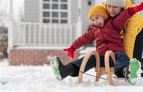 a bigger sister rides her brother on a sled in front of their house in