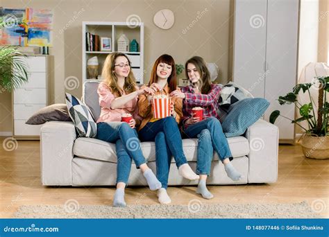 Three Beautiful Young Women Friends At Home Eating Popcorn Sitting On