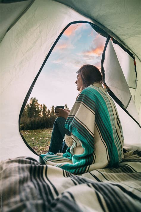 Female Camper Sitting At The Entrance To Her Tent With Coffee At Dawn