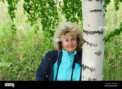 55 60 Year Old Woman Stands Against The Background Of Birch Branches