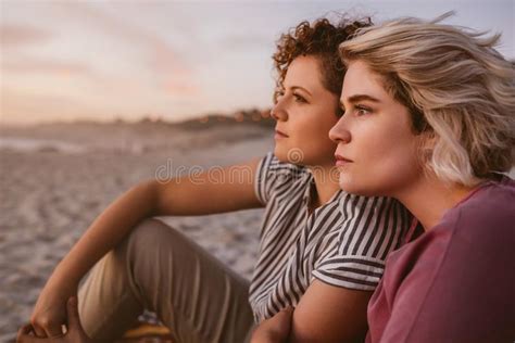 Content Lesbian Couple Sitting Together On The Beach At Dusk Stock