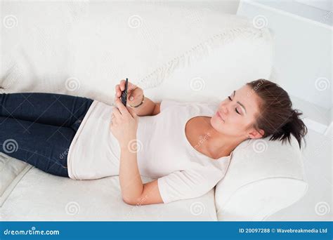 Jeune Brunette Texting Tout En Se Trouvant Sur Son Sofa Photo Stock
