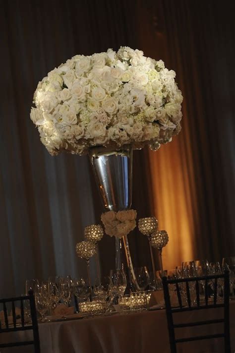 A Tall Vase Filled With White Flowers Sitting On Top Of A Table Next To