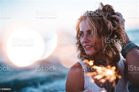 beautiful boho girl celebrating with sparklers at beach at sunset stock