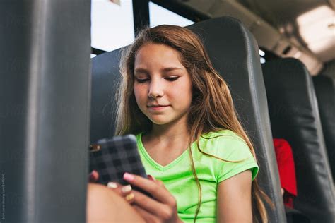 School Bus Girl Riding Bus Checks Cell Phone By Stocksy Contributor