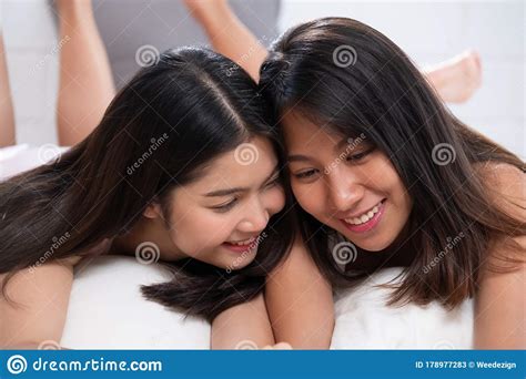 Asian Lesbian Couple Lying Down On Bed Holding Hand And Chatting In
