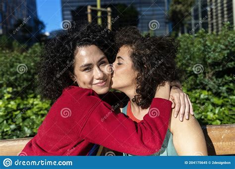 Smiling Lesbian Couple Embracing And Relaxing On A Park Bench Stock