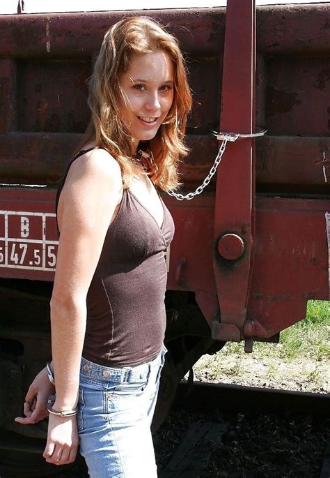 smiling lady in brown top and denim jeans handcuffed behind her back her neck chained to a