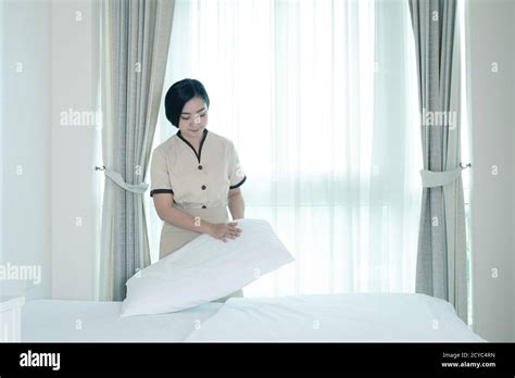 Young Beautiful Asia Maid Arranging Pillow On The Bed In Hotel Room