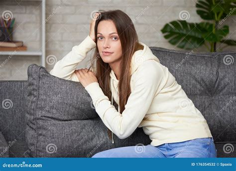 Pretty Woman Is Smiling And Sitting On A Sofa In Living Room Stock