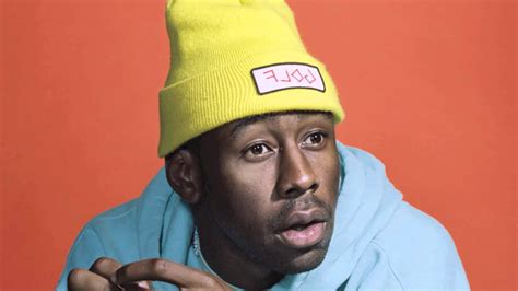 tyler  creator   light orange background wearing blue cap tshirt