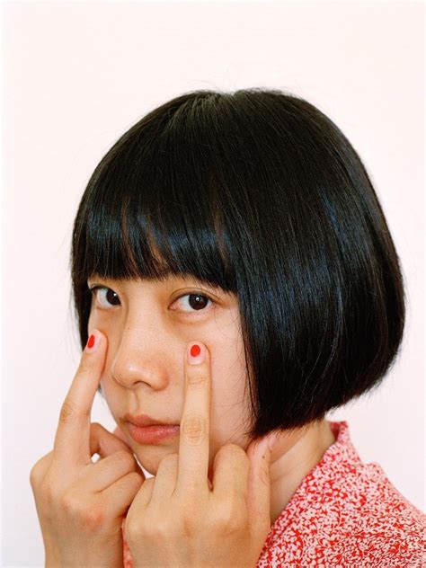 a woman with black hair and red nail polish holding her finger up to