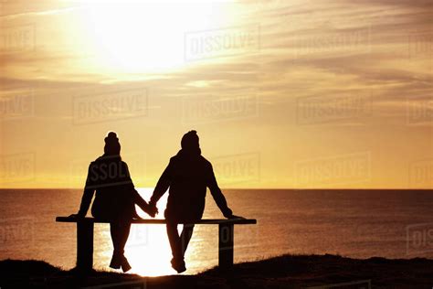 silhouette of couple sitting on bench holding hands