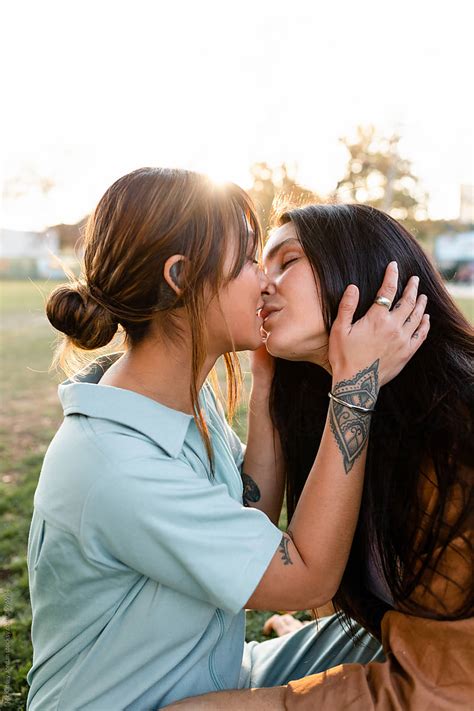 beautiful lesbian couple lovingly kiss while sitting on a park bench